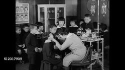 1939: JAPANESE EDUCATION: WS School entrance elementary children standing by gate. WS Young children entering building. INT VS Female doctor examining children's mouths. VS Children in kindergarten drawing. MS Boy writing characters. Tokyo Japan Instructional Video