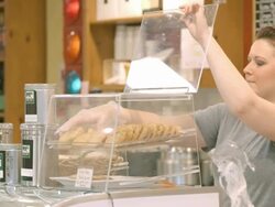 female coffee house barista wearing protective glove places chocolate chip cookies into pastry display case / Redlands, California, USA Stock Footage