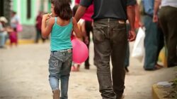 Young girl with balloons holds hands with father while walking up crowded cobblestone street Stock Footage
