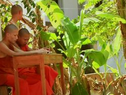 MS SLO MO Shot of two young Buddhist monks in saffron robes sitting on bench and another one standing / Luang Prabang, Laos Stock Footage