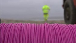 A construction worker walks toward a beach as fuse lines roll on a spool. Stock Footage