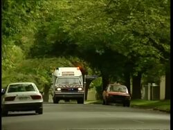 MS pan right, Ambulance rushes along leafy, suburban street, Australia Stock Footage