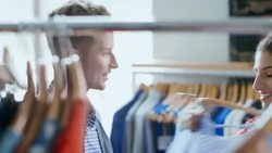 Girl holds up shirt and poses for smartphone selfie with friend in trendy clothing shop Stock Footage