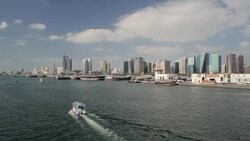 A covered ferryboat sails past commercial vessels on the shoreline of Dubai's Deira district. Stock Footage