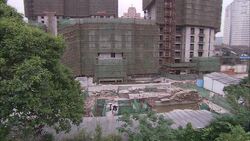 A construction worker pushes a wheelbarrow past buildings with scaffolding in Shanghai, China. Stock Footage