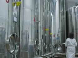 MS TS young woman in white lab coat walking along row of stainless steel tanks, stopping at last tank, looking up and taking notes on clipboard, exits frame right RED R3D 4K Stock Footage