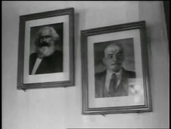 B/W 1950s PAN from framed portraits of Marx + Lenin on wall to Soviet flag / newsreel Stock Footage