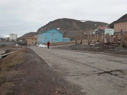 A man walking down a street in Barentsburg, a Russian mining settlement on Svalbard archipelago; some buildings are visible in the back Stock Footage