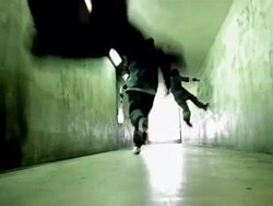Low angle long shot three freerunners running down hallway away from CAM / jumping off walls Stock Footage