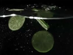 Lime slices drop falling into water, black background Stock Footage