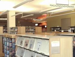 WS PAN display racks of magazines and newspapers in public library as gentleman walks up to daily newspaper section and retrieves paper to read / Rancho Mirage, California, USA  Stock Footage