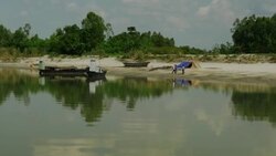 View from a noisy wooden boat approaching a small settlement on a sandy river bank in Bangladesh Stock Footage