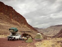 WS ZO T/L View of Desert with breaking camp in rugged valley with tents, built shelter, all terrain vehicle, equipment and people / Windhoek, Namibia Stock Footage