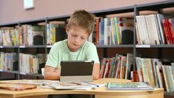 DS Boy sitting in library and using a tablet Stock Footage