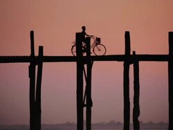 LS A young boy cycles across U Bein bridge at sunset, the longest teak bridge in the world / Mandalay, Myanmar Stock Footage