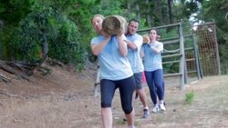 Team racing with logs on boot camp obstacle course Stock Footage
