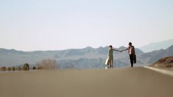 Young couple stroll up a desert road in the sweltering heat Stock Footage