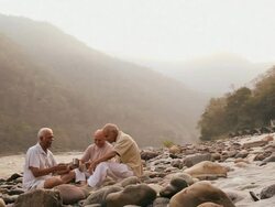 Three senior men drinking tea at riverbank, Ganges River, Rishikesh, Uttarakhand, India Stock Footage
