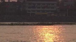 Longboats cruise past buildings on the shore of the Mekong River, Cambodia. Stock Footage
