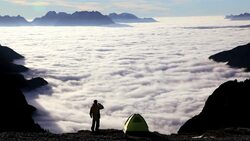 A hiker squats next to his tent and overlooks the clouds drifting around the peaks in the Italian Dolomites. Stock Footage