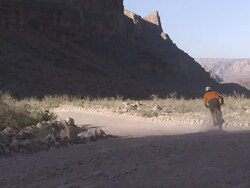 Low Angle static - A bicyclist pedals along a narrow dirt road in the Grand Canyon / Arizona, USA Stock Footage