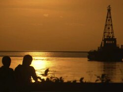 Long Shot Locked Down - Silhouetted couple cuddle and talk while looking at the golden, shimmering bay / Manilla philippines Stock Footage