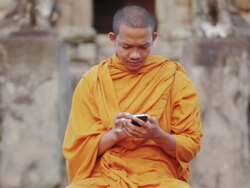 CU A Buddhist monk taps on the screen of a smartphone on an ancient temple in Angkor Wat / Siem Reap, Cambodia Stock Footage