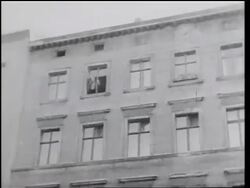 B/W 1961 tilt down man throwing belongings from building window then jumping into net on ground / Berlin Stock Footage