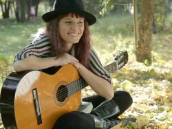 Young woman wearing hat posing in park outdoors, holding guitar. Stock Footage
