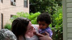 MS Teenage girl holding infant sister on backyard patio with family on summer evening Stock Footage
