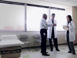 WS Three doctors standing in discussion looking at smart phone in exam room/Seattle, Washington, USA Stock Footage