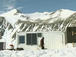 WS of ALE staff member walking into weather station cabin with snowy mountains / Union Glacier, Heritage Range, Ellsworth Mountains, Antarctica  Stock Footage