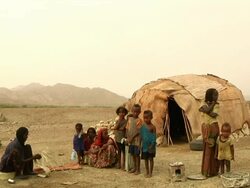 Family standing next to straw and wooden hut with woman braiding straw Stock Footage