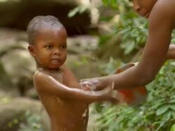 MS Shot of little boy being washed in river by her mother / Fouta Djalon, Guinea Stock Footage