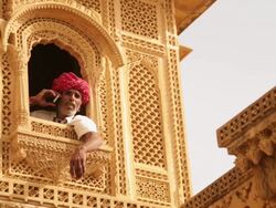 Rajasthani senior man talking on a mobile phone at window, Amar Sagar Jain Temple, Jaisalmer, Rajasthan, India Stock Footage