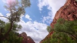 Camera tilts up from fast running river to red-rock mountain tops against blue cloud-filled skies Stock Footage
