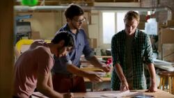 Shop owner spreads papers out on workbench and picks up tablet to instruct workers Stock Footage