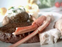 SLO MO ECU PAN View of crab legs dropping into plate with steak and baked potatoe or lemons, tomatoes, and lettuce in background / Los Angeles,CA,USA Stock Footage