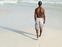Man walking on sandy beach into the sea Stock Footage