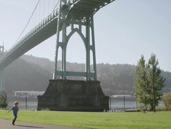 WS PAN Shot of boy running through park as large St. Johns bridge looms behind him / Portland, Oregon, United States Stock Footage