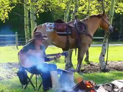 Cowgirl playing Guitar around campfire with horse Stock Footage
