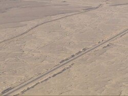 Long Shot, pan-left tilt-down - A road across the Sahara Desert leads to a gate and a fortress / Egypt Stock Footage