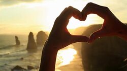 Person frames Twelve Apostles at sunset into heart shape Stock Footage