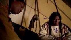 Male and female Native American Indian sitting in teepee sharpening stick with knife Stock Footage