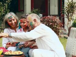 Senior man feeding rasgulla to his granddaughter in holi festival  Stock Footage