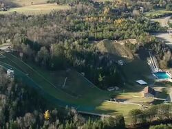 MS AERIAL ZI Flag blowing with wind near Olympic Ski Jumps at Placid lake / New York, United States Stock Footage