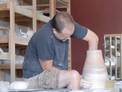 MS potter in pottery studio at pottery wheel reaches with his arm into tall vase while shaping / Palm Springs, California, USA Stock Footage