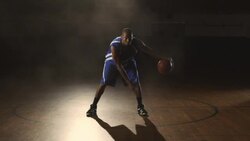 A focused male basketball player dribbles a basketball between his legs on a gym court. Stock Footage