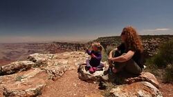 Mother and young daughter rest on the rim of the Grand Canyon while little girl eats apple Stock Footage
