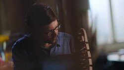 Artist works on furniture design on laptop computer as craftsman chisels in wood shop Stock Footage